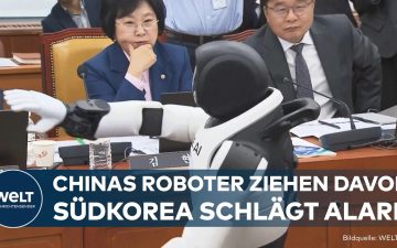 Zwei humanoide Roboter tanzen vor Politikern im südkoreanischen Parlament, im Hintergrund Abgeordnete