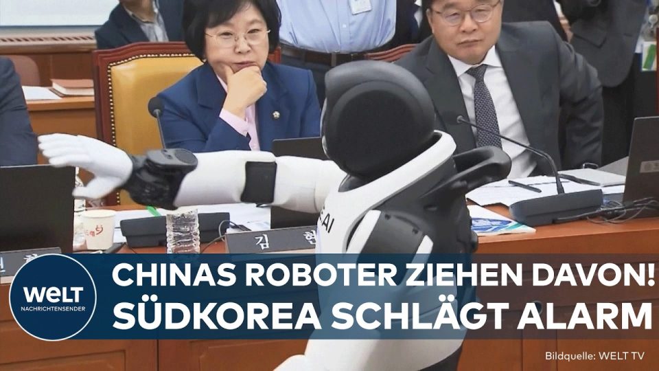 Zwei humanoide Roboter tanzen vor Politikern im südkoreanischen Parlament, im Hintergrund Abgeordnete