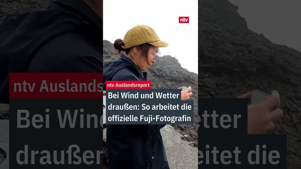 Fuji-Fotografin Megumi Da steht mit Winterjacke und Kamera bei Nebel am Gipfel des Mount Fuji