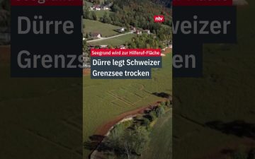 Trockengefallener Seegrund des Lac de Brûlé mit „HELP"-Schriftzug im Gras – Symbol der Lac de Brûlé Dürre