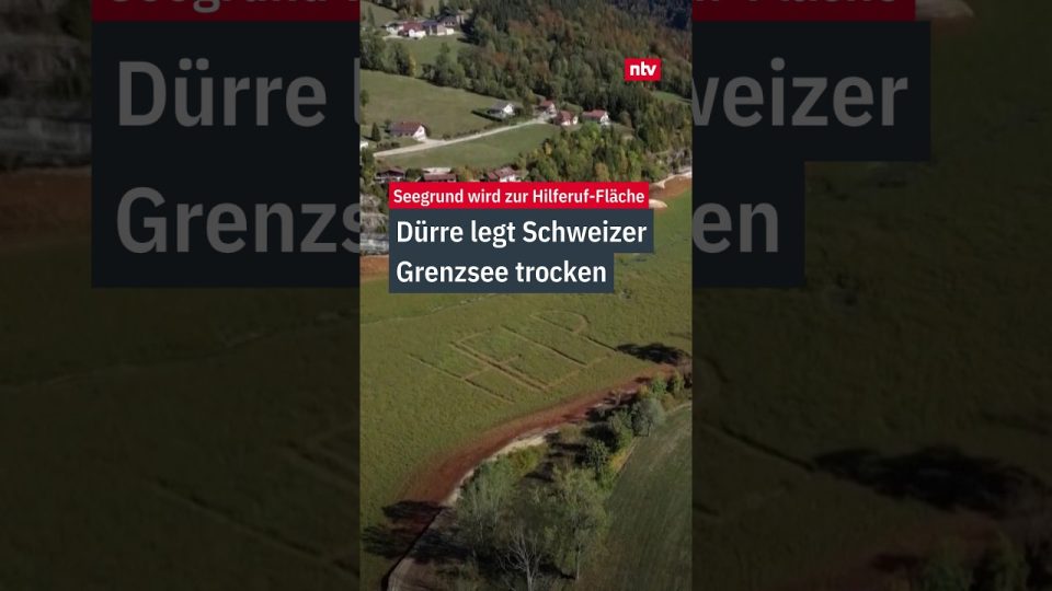 Trockengefallener Seegrund des Lac de Brûlé mit „HELP"-Schriftzug im Gras – Symbol der Lac de Brûlé Dürre